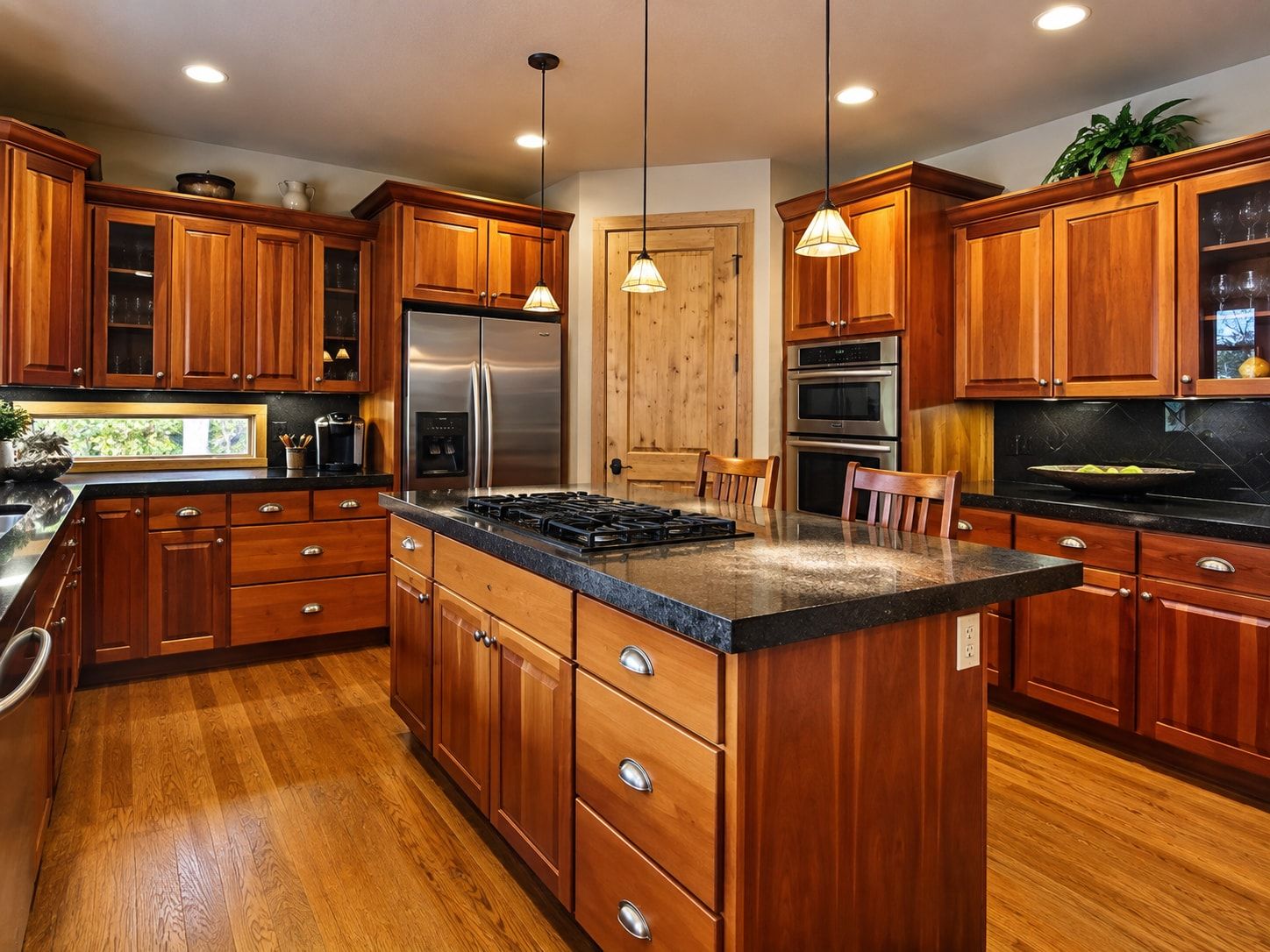 Kitchen with reddish wood cabinets, black granite countertops, and an island with a gas cooktop.
