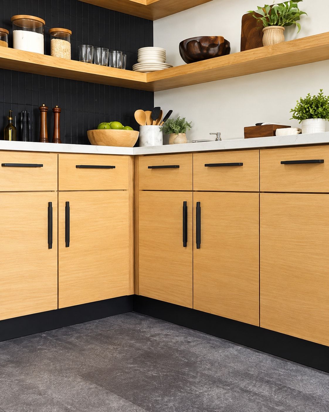 Corner of a kitchen with flat natural oak cabinets, long black handles, and a white countertop.